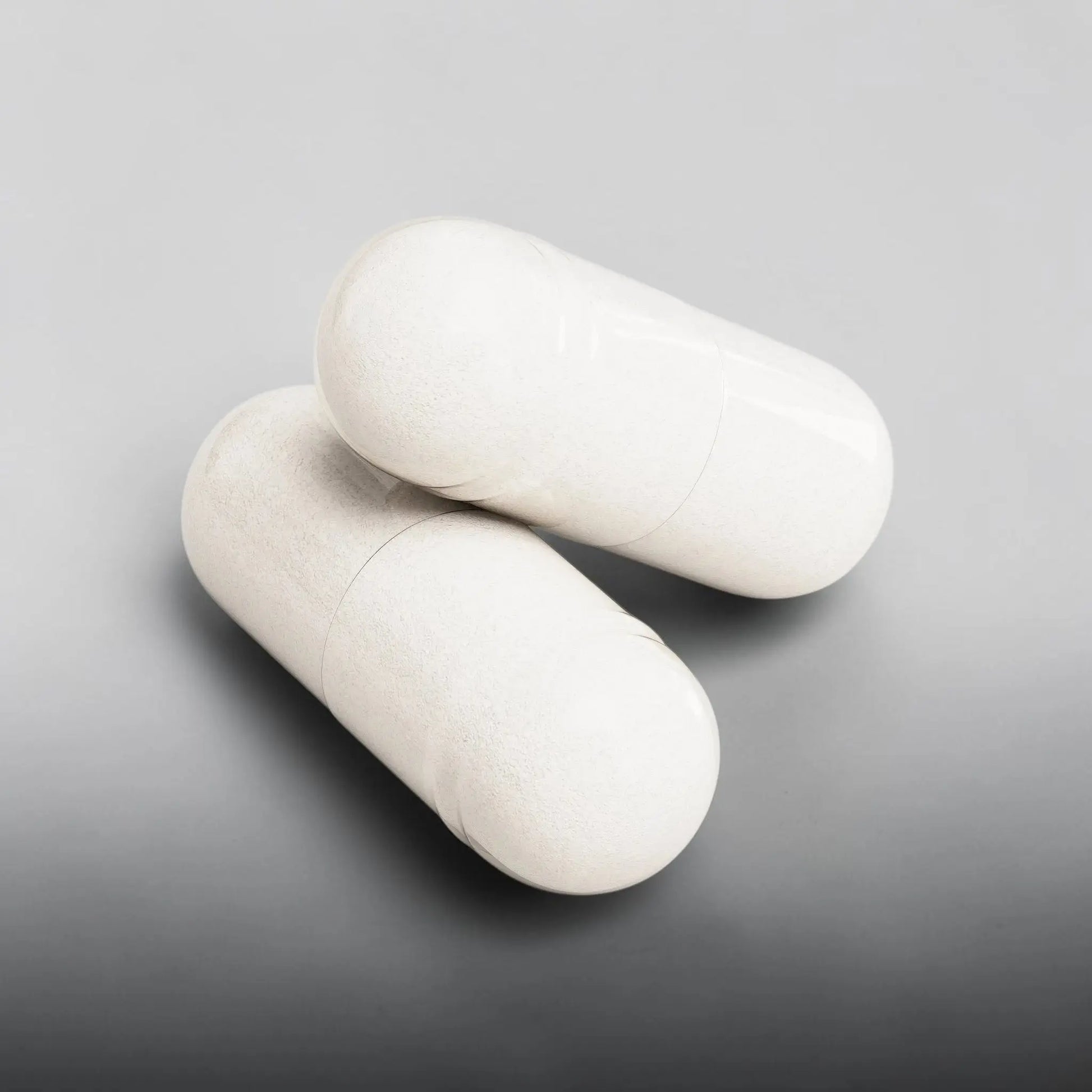 Deux gélules de magnésium glycinate AlphaVIT blanches sur fond blanc pour le soutien musculaire et la relaxation.
